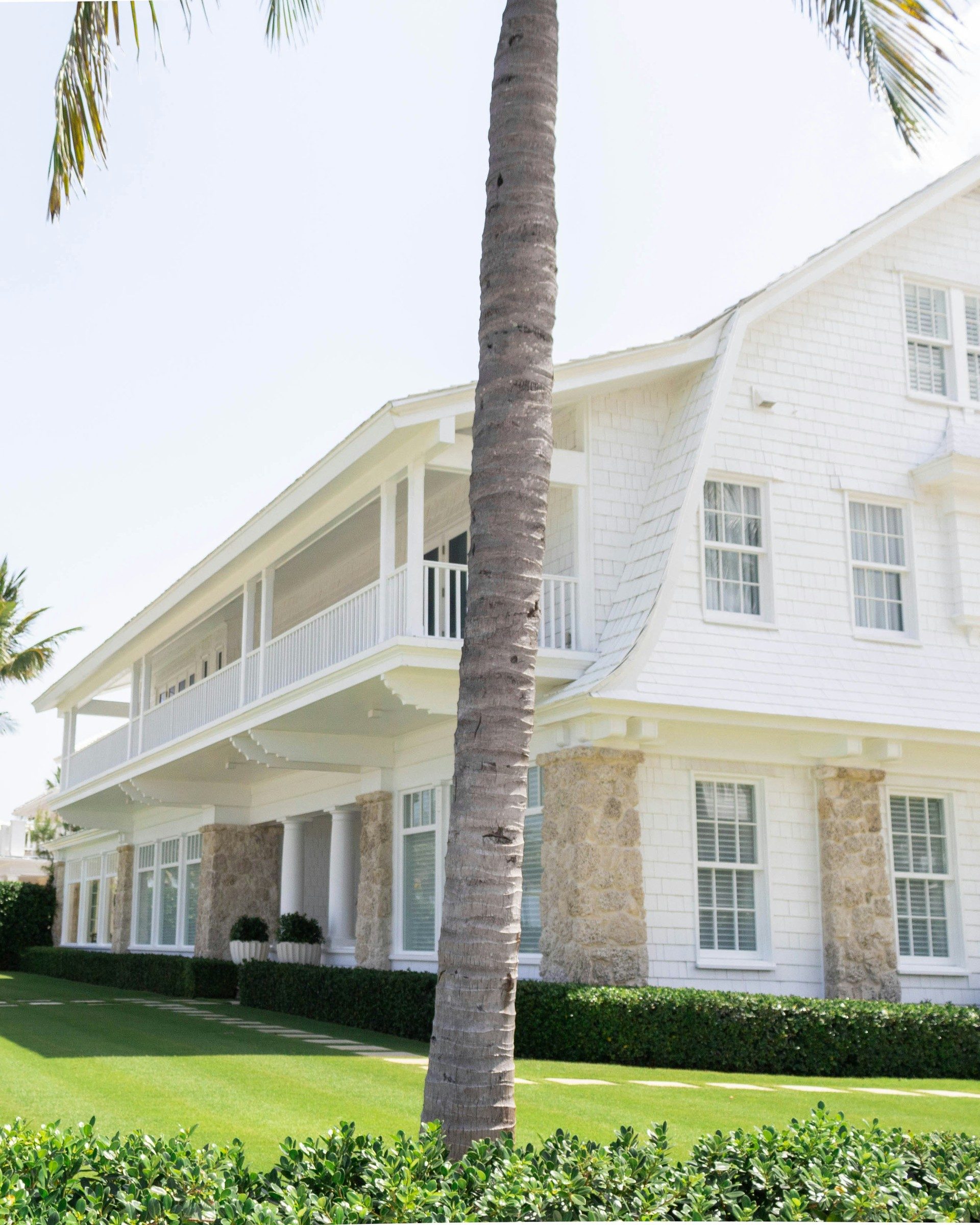 A white shingle-style home with palm trees and a manicured lawn